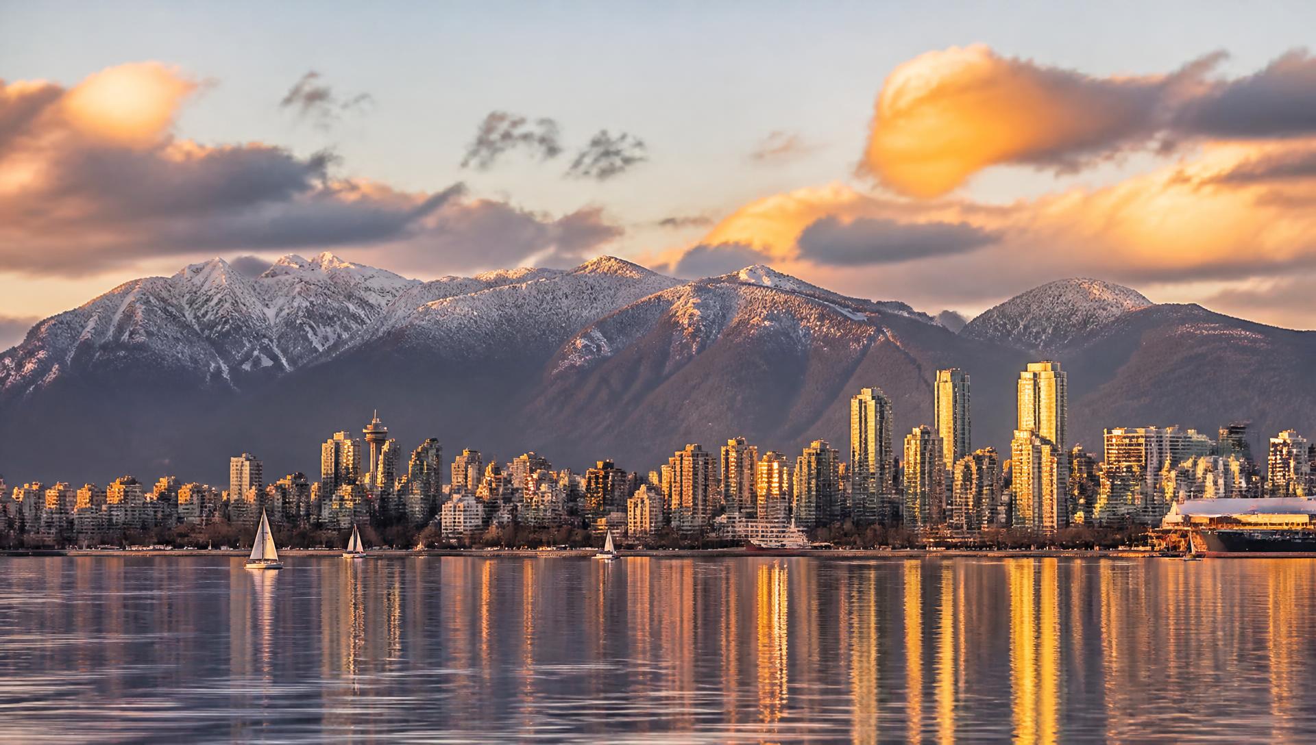 Skyline de Vancouver refletido na baía ao pôr do sol, com montanhas nevadas ao fundo